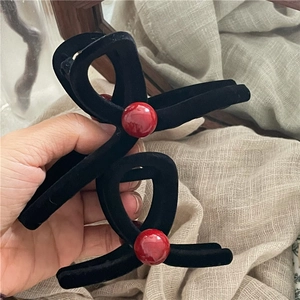 Dettaglio molletta per capelli nera floccata con sfere rosse su sfondo in tessuto beige