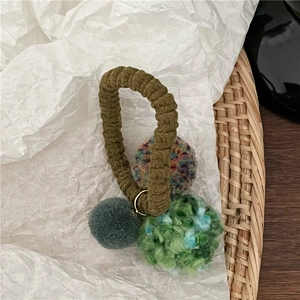 Detail view of colorful knit plush pom-poms on a green elastic hair tie with metal ring