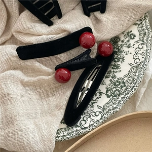 Dettaglio di fermagli per capelli in velluto nero con perle rosse su un piatto