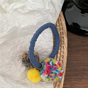 Detailed shot of elastic hair tie featuring colorful plush pom-poms and knitted yarn ball