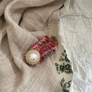Close-up of a handmade woven bow hair clip with a vintage pearl and golden metal center