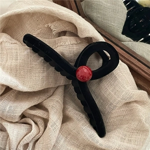 Dettaglio della molletta per capelli nera opaca con perla rossa su tessuto beige