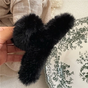 Close-up of black plush faux fur hair claw clip held over a cozy knit background