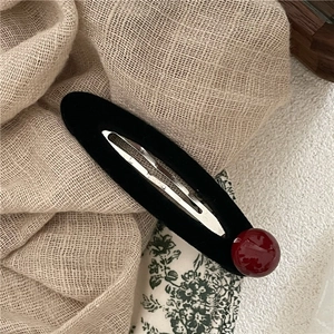 Macro di una clip per capelli vintage in velluto nero con una perla rosso intenso decorativa