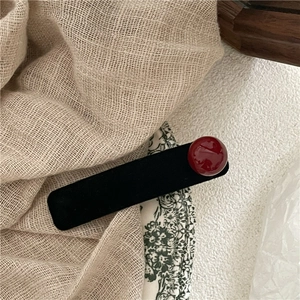 Dettaglio di un fermaglio vintage in velluto nero con perla rossa su sfondo di lino
