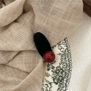 Dettaglio molletta capelli ovale nera floccata con una perla rosso scuro lucida decorativa