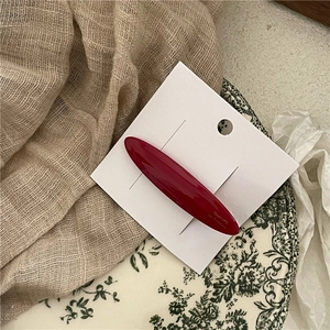 Close-up of a deep red acetate hair barrette with gold lettering on a display card