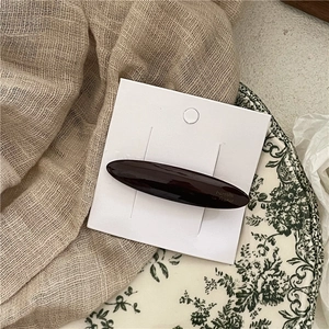 Close-up of a vintage dark brown acetate barrette on white display card with floral background