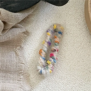 Détail de l'élastique en laine beige avec pompons colorés sur un fond en lin doux