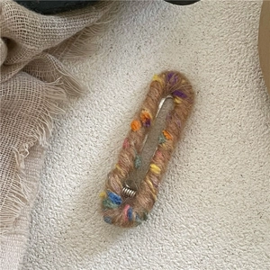 Détail de la barrette en laine avec pompons colorés sur fond de tissu en coton beige