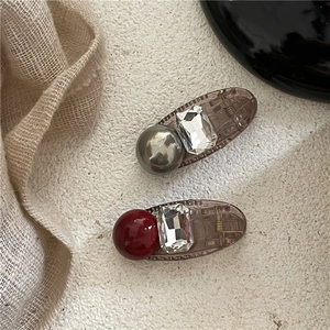 Détail de barrettes en perles rouge et grise avec strass sur tissu texturé beige