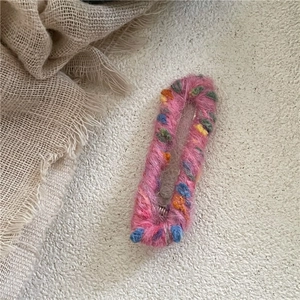 Détail d'une pince à cheveux en laine rose avec des boules colorées et tissées
