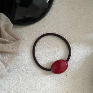 Detail view of a glossy red oval bead on a black elastic hair tie over white background