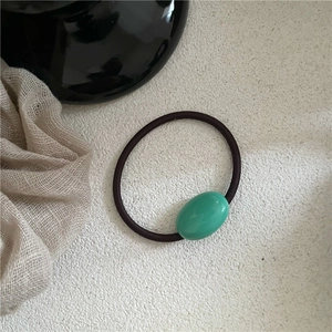 Macro view of a dark brown elastic hair tie featuring a smooth green oval resin bead