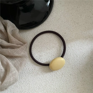 Close-up of cream oval pebble hair tie with brown elastic rope on minimalist background