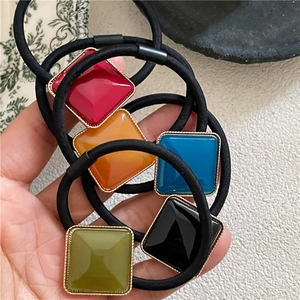 Detail of square acetate hair ties with golden edges in red, blue, and black colors
