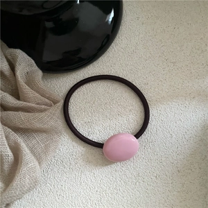 Close-up of pink oval pebble hair tie with dark brown elastic cord on a textured base