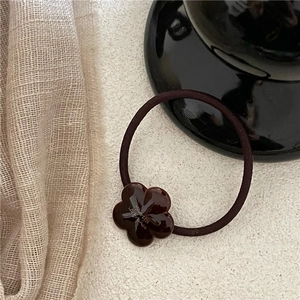 Detailed close-up of dark brown flower hair tie with resin accent and golden lettering