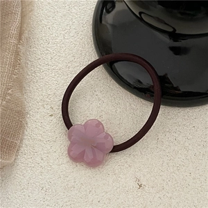 Close-up of pink acetate flower hair tie with dark elastic band on a textured surface