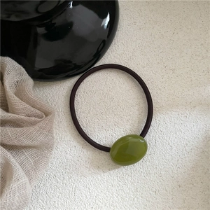 Detail view of cream olive green oval pebble hair tie with glossy resin on textured surface