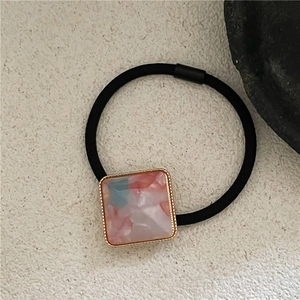 Detail of square resin charm with gold border on a high-elastic black ponytail holder