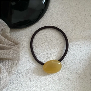 Detail of amber-colored resin pebble bead on high-elastic brown hair tie with soft texture