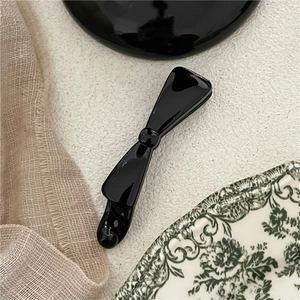 Close-up of a glossy black bow banana clip on a stylish decorative display background