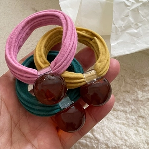 Three-piece set of cream-colored elastic hair ties with dark amber resin beads in hand