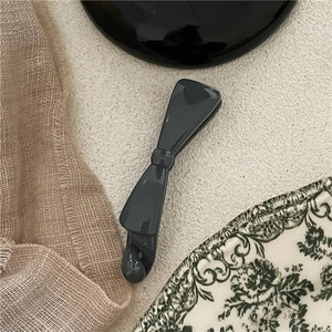 Close-up of a glossy dark grey bow-shaped banana hair clip on a vintage background