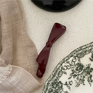 Deep red bow banana hair clip on a minimalist textured surface with vintage aesthetic