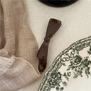 Detailed view of coffee brown bow banana hair clip on vintage fabric and ceramic plate