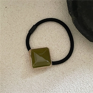 Close-up of olive green geometric square hair tie with gold trim on stone texture