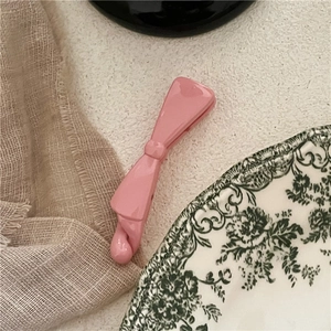Pink bow banana clip with a glossy glaze finish on a rustic fabric background