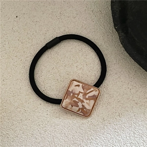 Detail of square marble acetate hair tie with golden metal edge on stone background