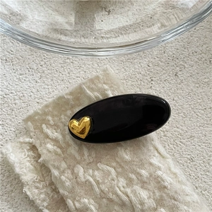 Détail d'une pince à cheveux ovale noire avec cœur doré sur fond en maille blanche