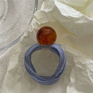 Close-up of lilac elastic towel scrunchie with an amber resin bead on textured paper