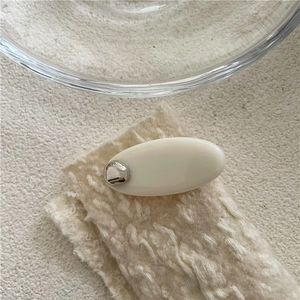 Détail de la pince à cheveux ovale crème avec goutte argentée sur tissu tricoté