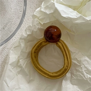 Close-up of mustard yellow elastic hair scrunchie with a large amber resin bead detail