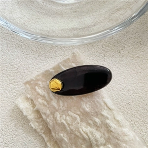 Vue macro d'une pince à cheveux ovale en acétate avec accent doré sur fond beige texturé