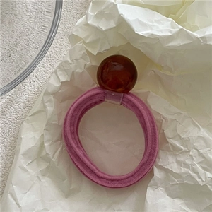 Detail of pink high-elastic hair tie with amber translucent geometric bead on white paper
