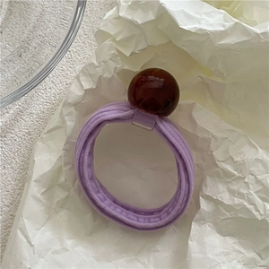 Close-up of a purple elastic hair tie with a dark amber resin bead on white art paper