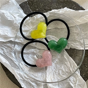 Detailed macro of resin heart charms in pink, green, and yellow on black elastic hair ties