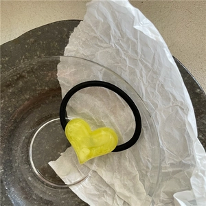 Detailed macro view of yellow heart-shaped acrylic charm with marble texture on black hair tie
