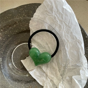 Detail view of a green heart pendant on a black elastic hair tie for ponytail styling