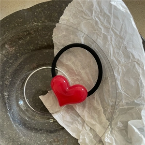 Close-up of a glossy red heart charm on a black elastic hair tie in a stylish glass dish