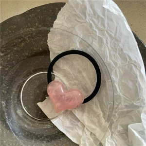 Detail of pink heart hair tie with marble texture on white paper and glass tray
