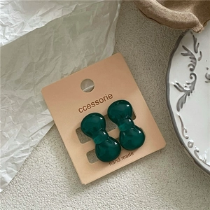 Detailed close-up of dark green bow-shaped resin earrings on a vintage paper card