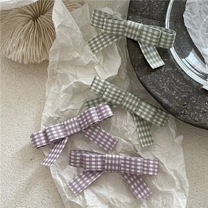 Detail showing green and purple plaid fabric bow hair clips on a white texture paper