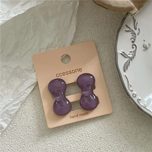 Detailed macro of small purple resin bow earrings on a handmade accessory card