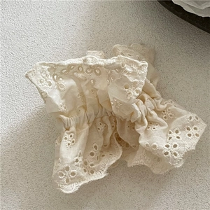 Makro-Detail von cremefarbenem Spitzen-Haargummi mit floraler Bestickung und Wellenrand